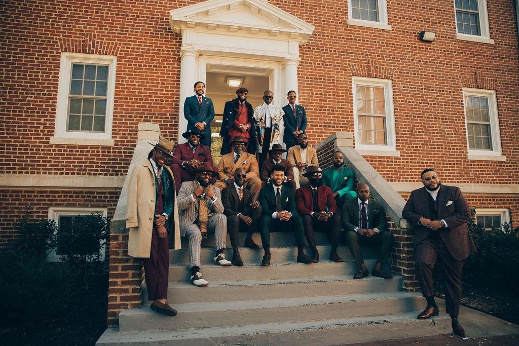 Black Menswear FlashMob — men in tailored suits gathered on the steps of a brick building